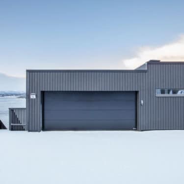 Mørk Hörmann garasje koblet til huset i et vinterlandskap